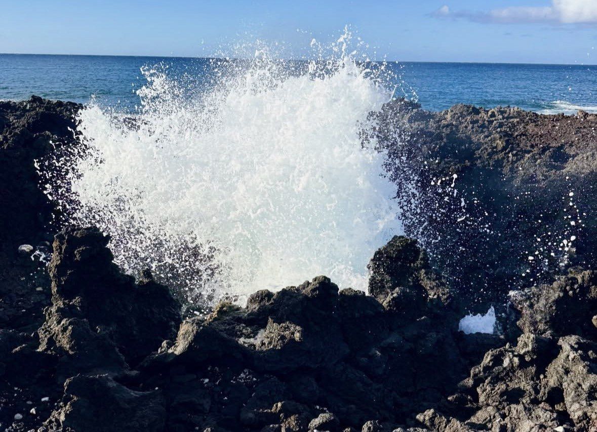 Seawater bursting from a blowhole in jagged black lava rock