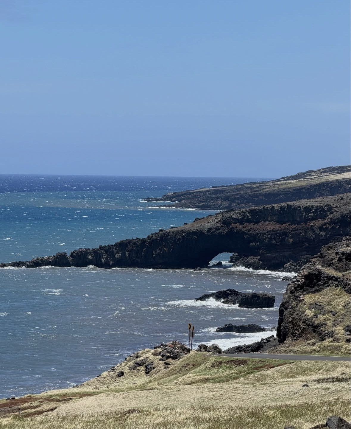 Sea arch in lava cliffs above dry golden grass on Maui's back road