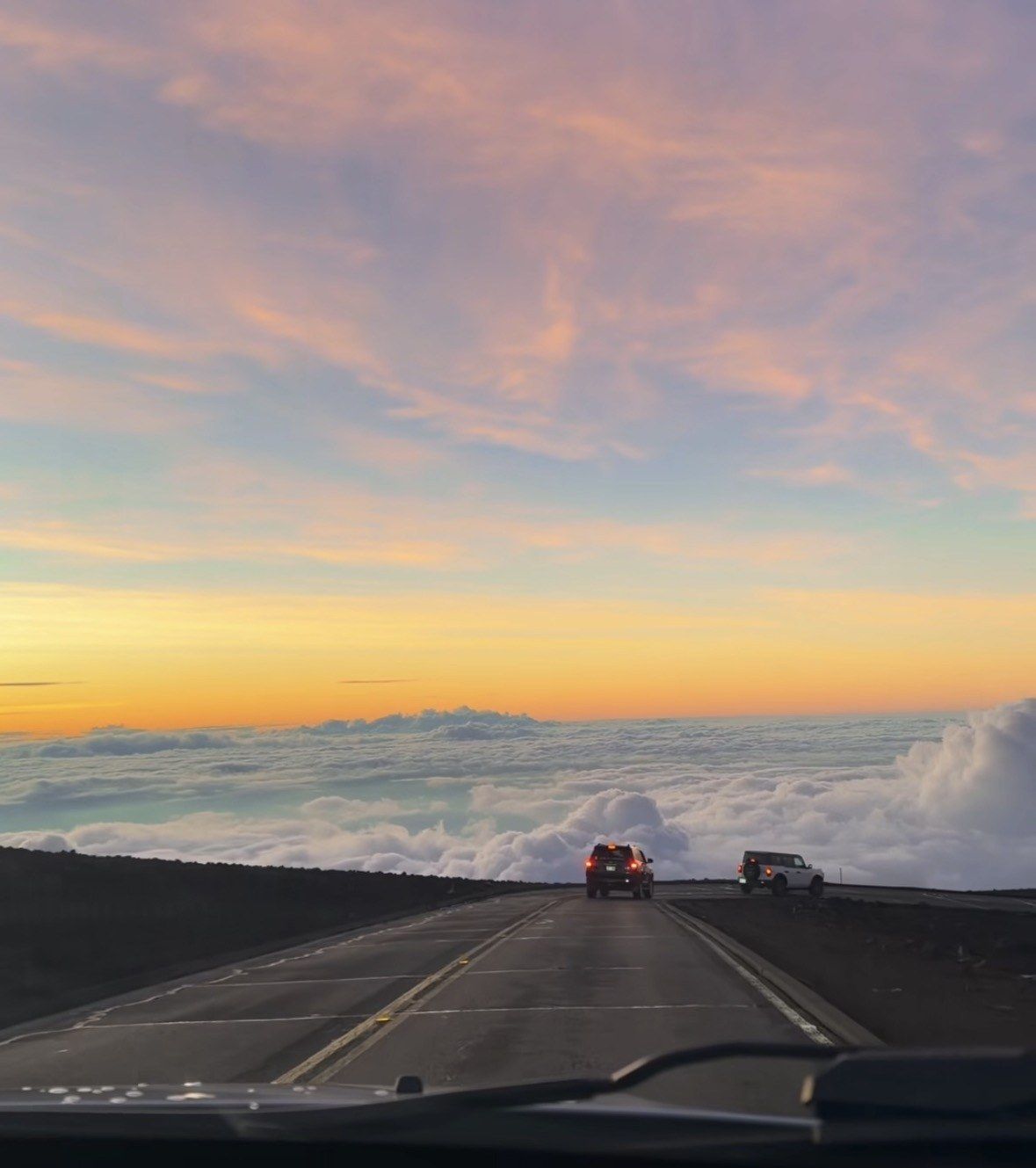 Cars on Haleakala summit road at sunrise above a cloud layer
