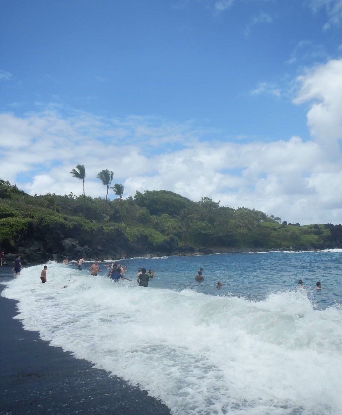 Swimmers in breaking surf at a black sand beach near Hana