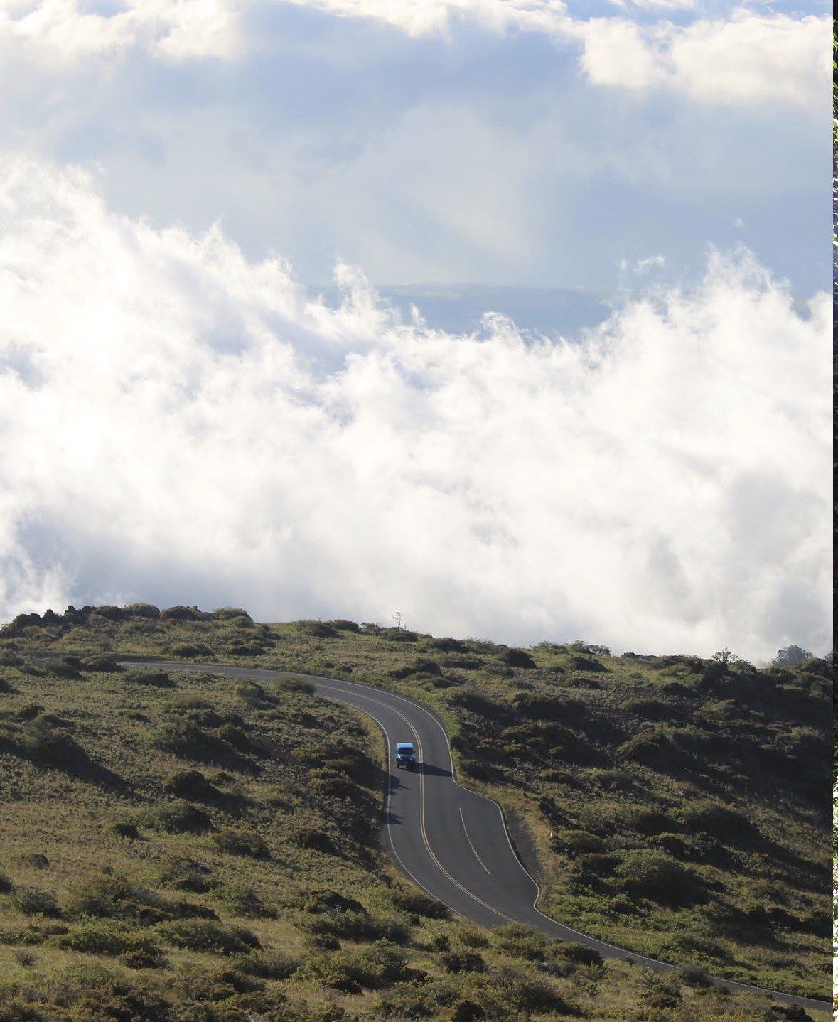 Lone car on a curving upcountry highway below banks of cloud